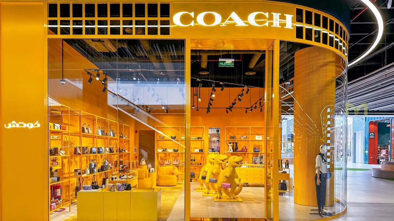 Bright yellow Coach store with dinosaur displays carrying handbags in a mall setting.
