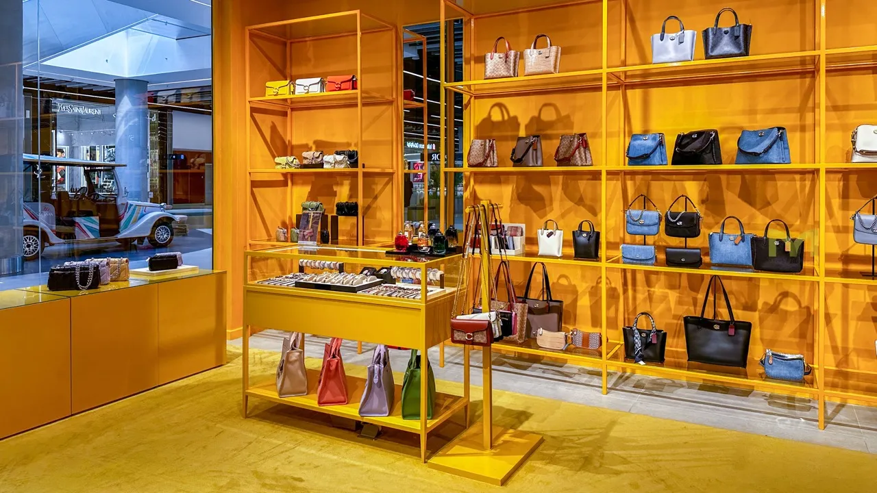 Retail store with yellow shelves and cabinets displaying handbags and accessories in various colors and styles.