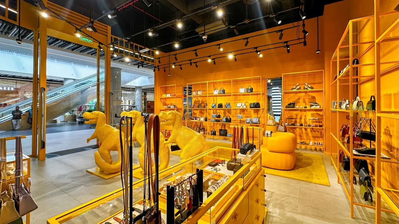 Bright orange retail store interior with handbags, shoes, belts, and three yellow dinosaur statues.
