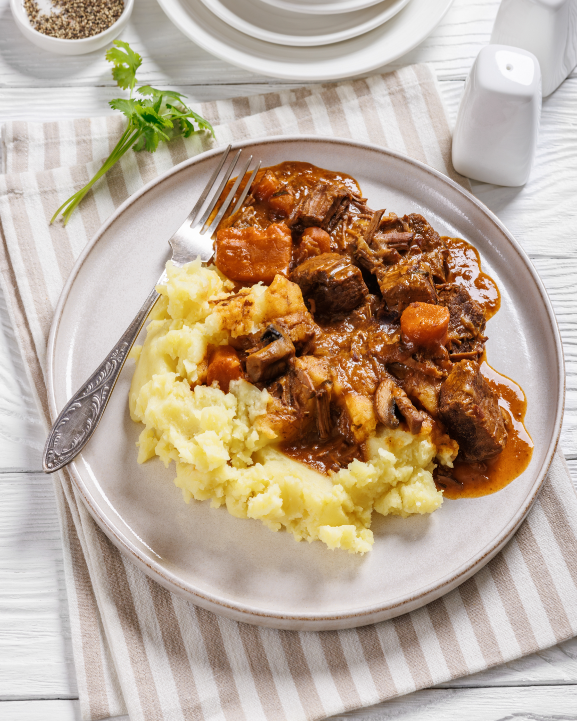 Assiette de purée de pommes de terre servie avec un ragoût de bœuf aux carottes et champignons.