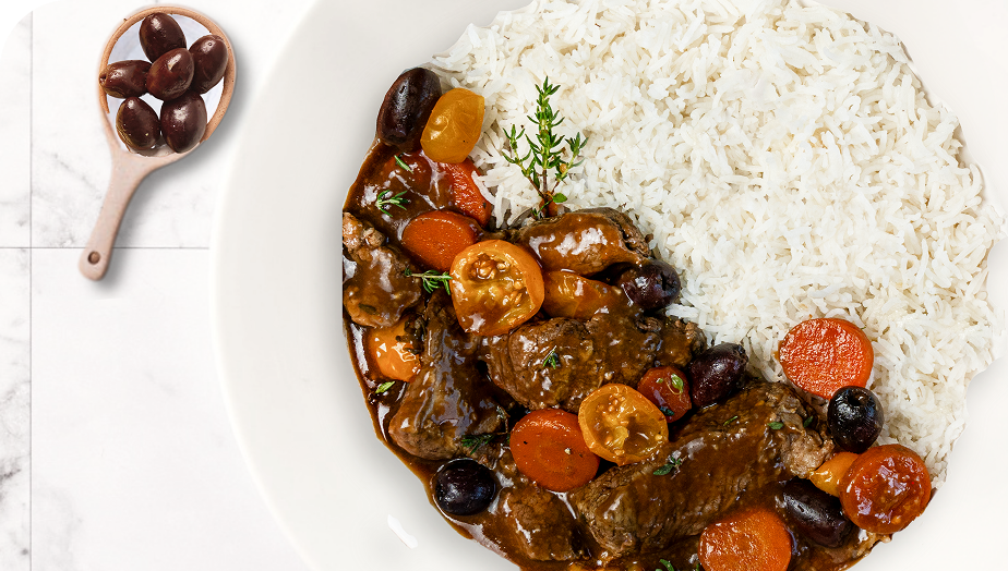 Assiette de riz blanc accompagné de ragoût de viande avec des carottes, des tomates cerises jaunes et rouges, des olives noires, et du thym frais.