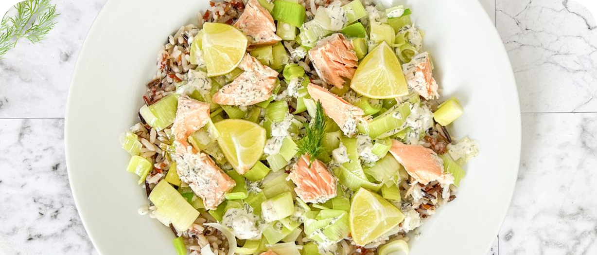 Assiette de riz sauvage avec morceaux de saumon, poireaux, quartiers de citron vert et sauce crème aux herbes.