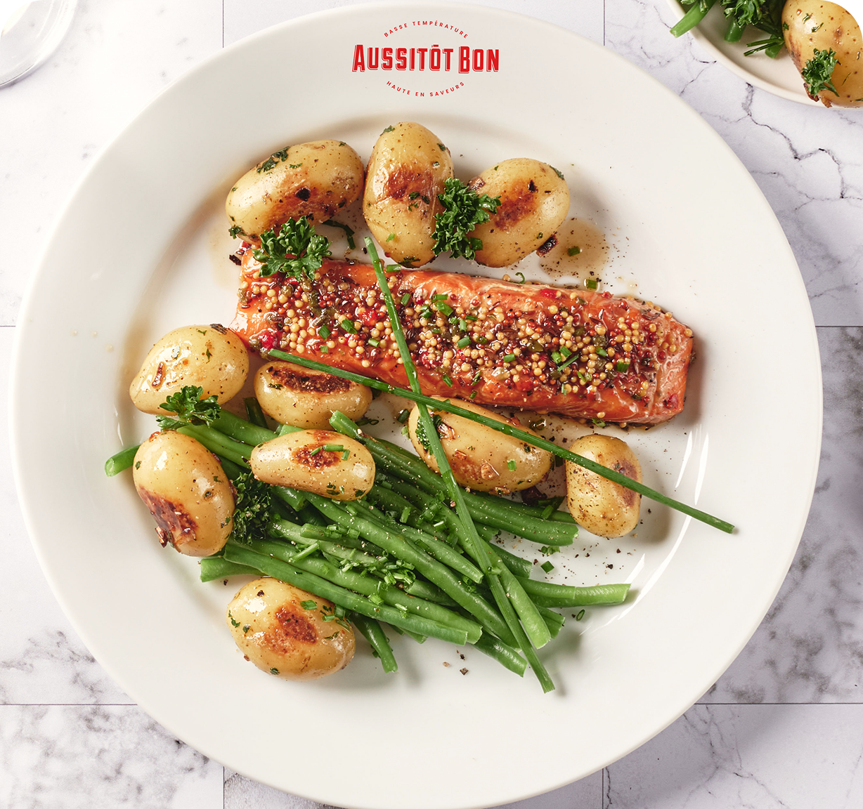 Filet de saumon avec graines de moutarde, pommes de terre rôties et haricots verts garnis de persil sur une assiette blanche.