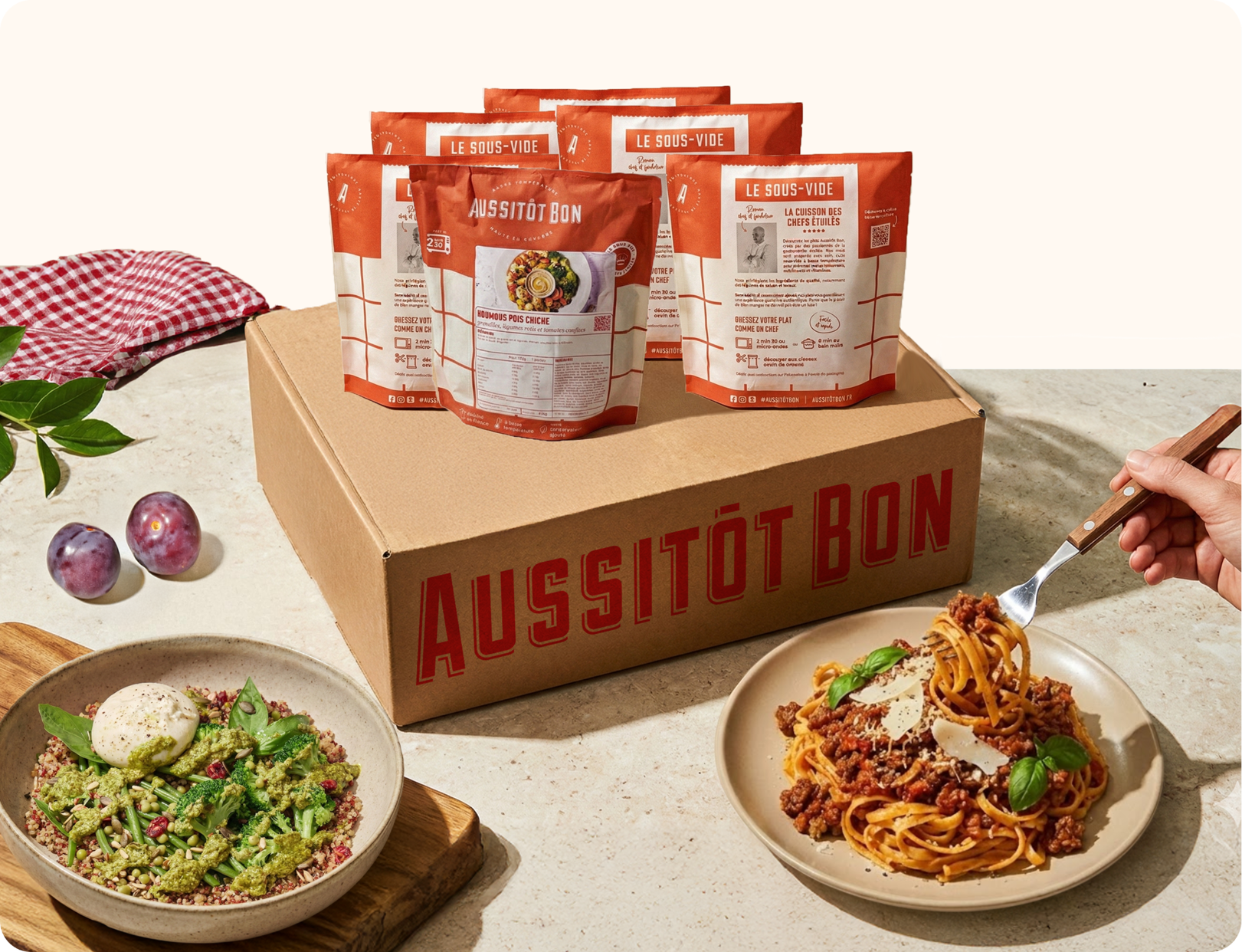 Boîte en carton Aussitôt Bon avec plusieurs sachets repas sous-vide, un plat de pâtes bolognaises garni de basilic et fromage, et un bol de salade avec une boule de mozzarella.