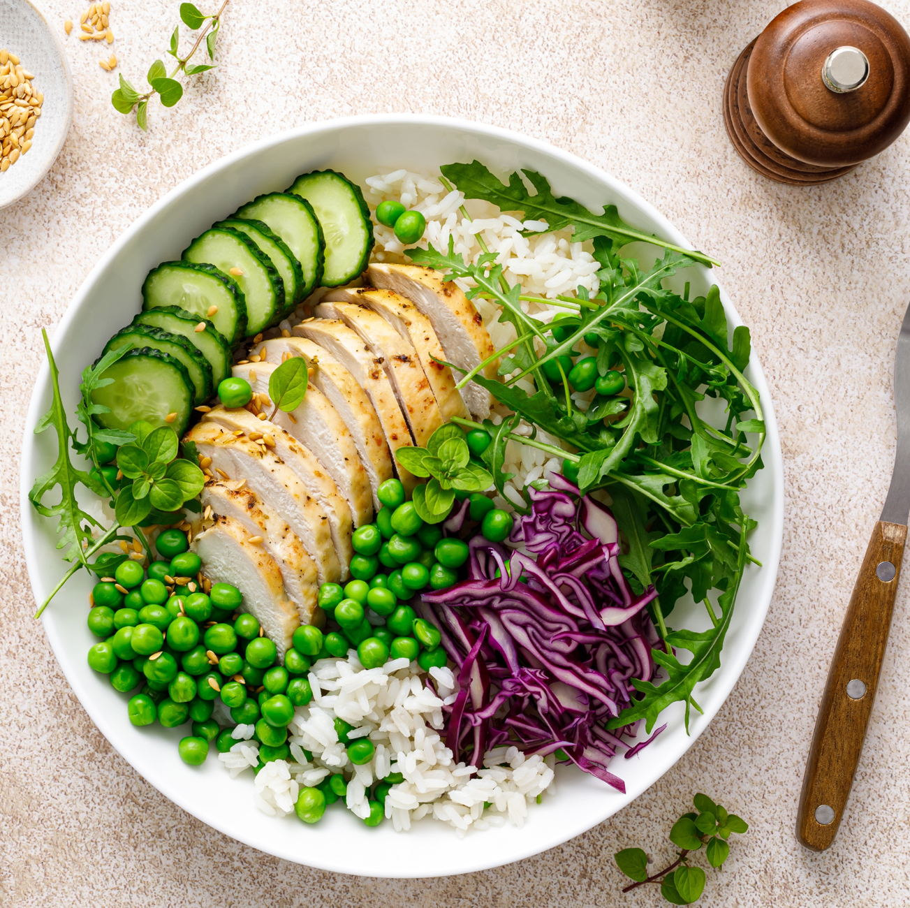 Bol de salade avec poulet grillé tranché, concombre, petits pois, riz blanc, chou rouge râpé et roquette.