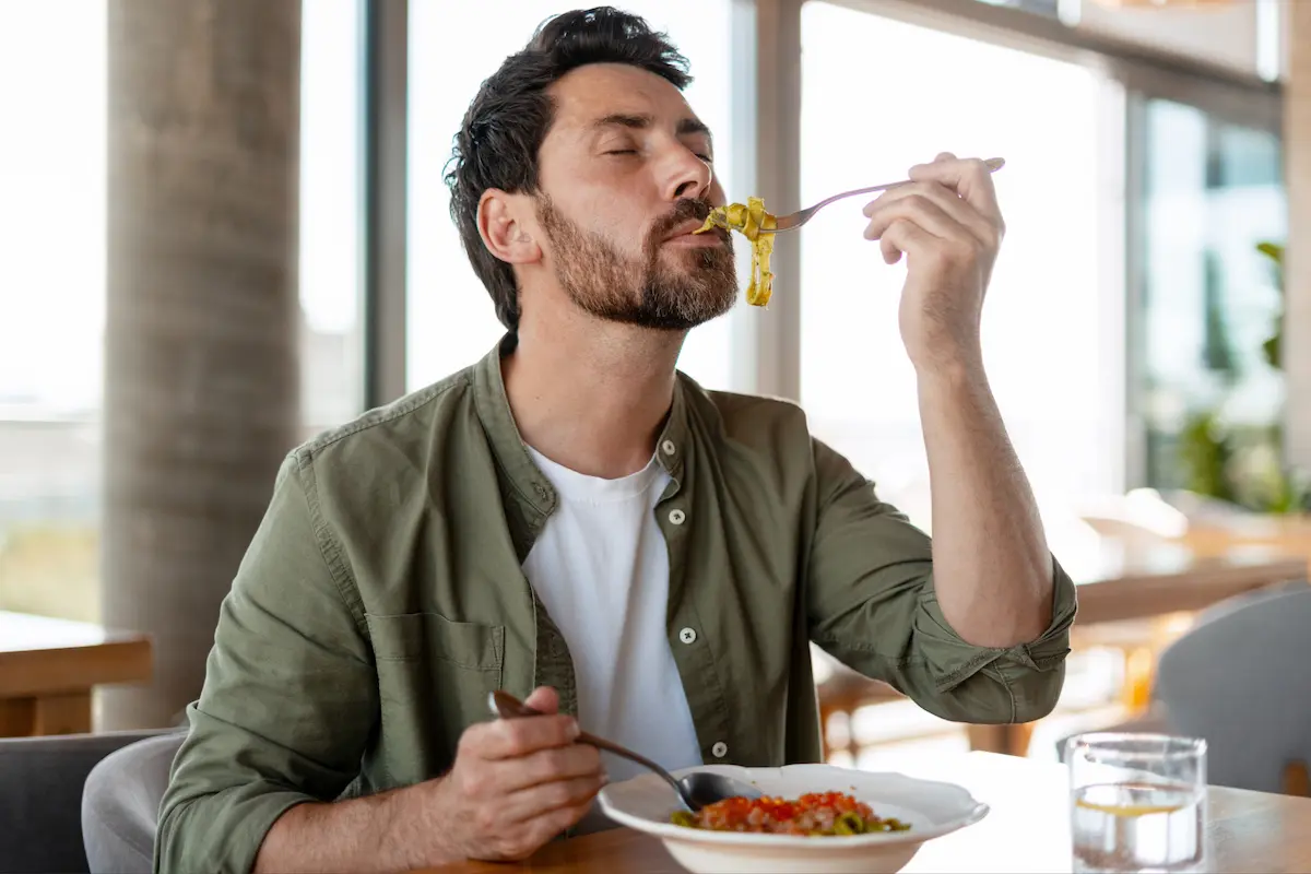 Homme appréciant un plat de pâtes dans un restaurant lumineux.