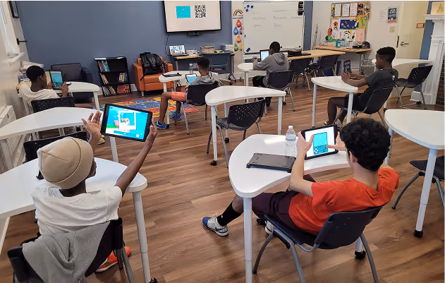 Students seated at individual desks in a classroom using tablets for learning activities.