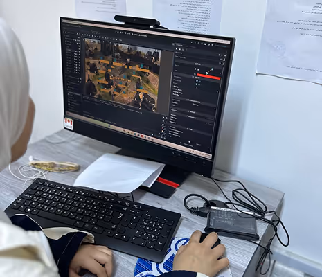Person working on a computer with game development software open on the screen showing a game scene and editing tools.
