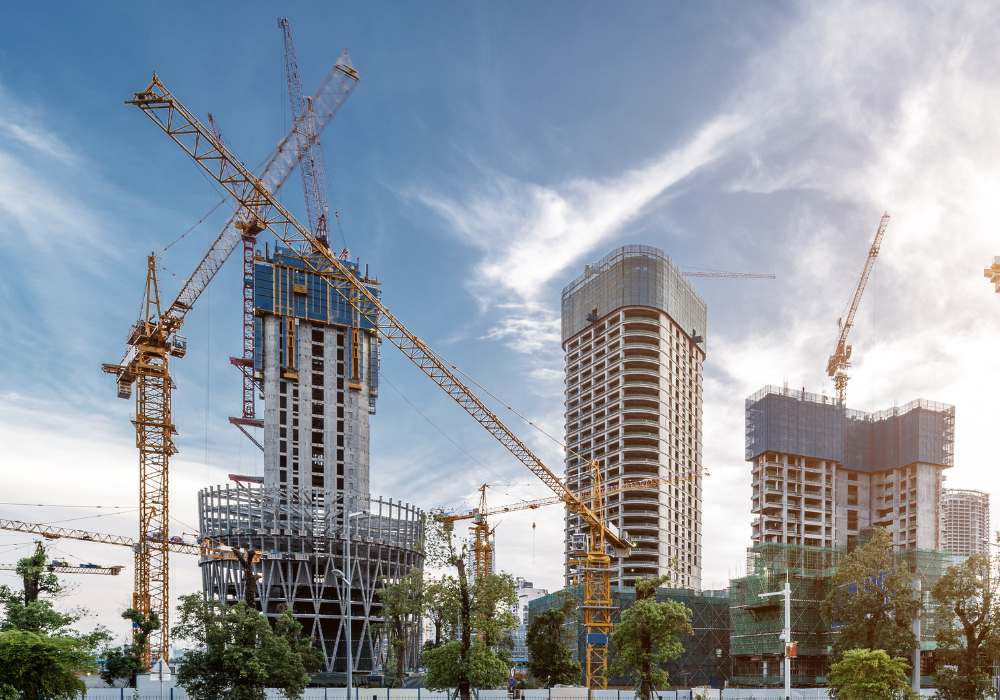 Multiple cranes and high-rise buildings under construction against a partly cloudy sky.