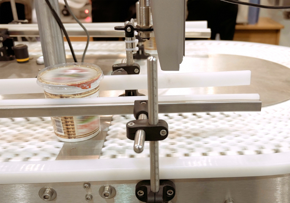 Plastic cup with sealed lid on a conveyor belt in an automated packaging process.