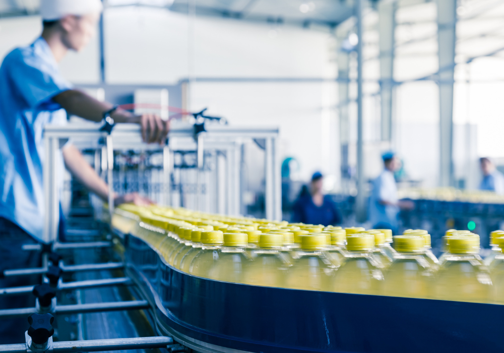Assembly line with numerous yellow-capped bottles filled with a yellow liquid, operated by workers in a production facility.