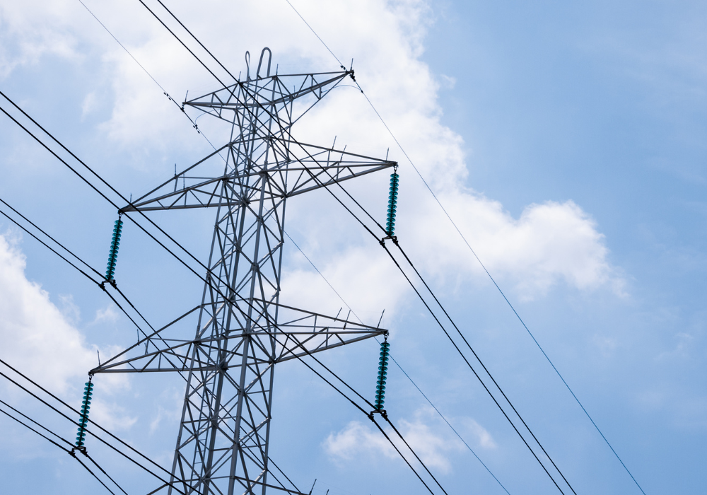 Steel electricity transmission tower with power lines against a partly cloudy blue sky.