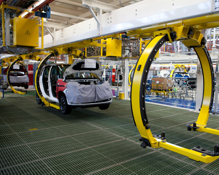 Car bodies in an automotive assembly plant hanging from a yellow overhead conveyor system.