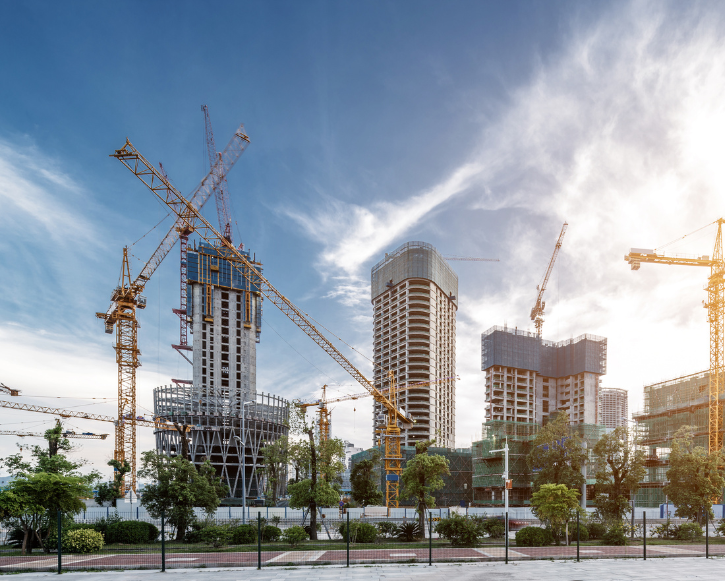Modern high-rise buildings under construction with multiple cranes and a partly cloudy sky.