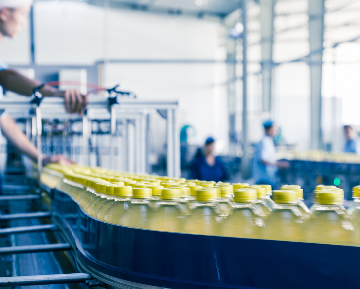 Rows of yellow-capped plastic bottles on a conveyor belt in a beverage production factory.
