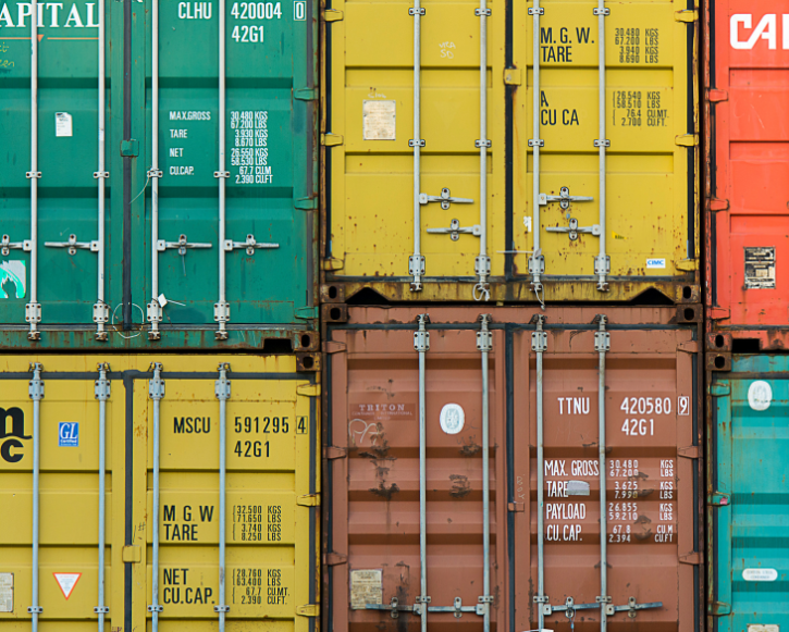 Stacked colorful shipping containers in green, yellow, orange, brown, and blue with visible metal locking bars and weight markings.