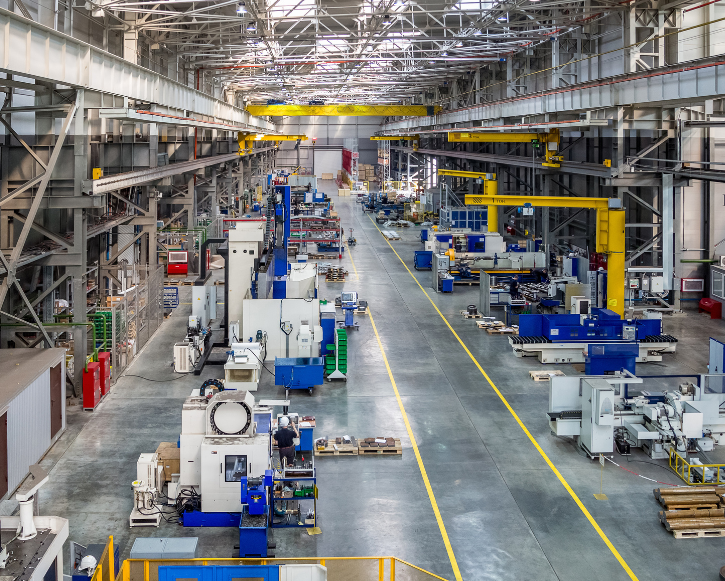 Spacious industrial manufacturing facility with machinery, yellow overhead cranes, and clear pathways.