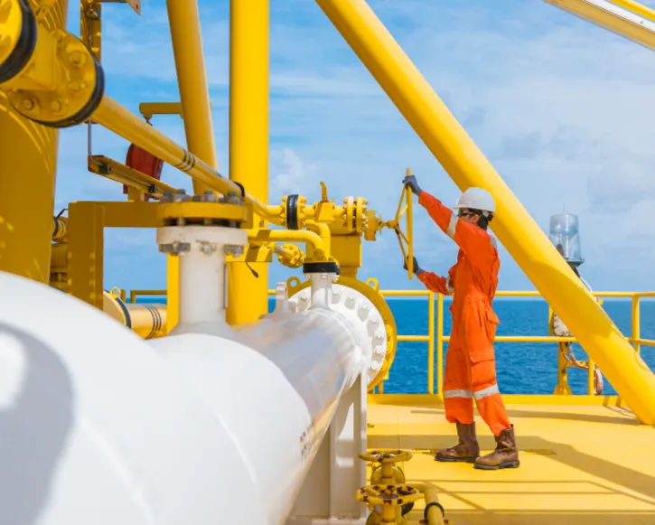 Offshore energy worker in orange coveralls operating a valve on a platform