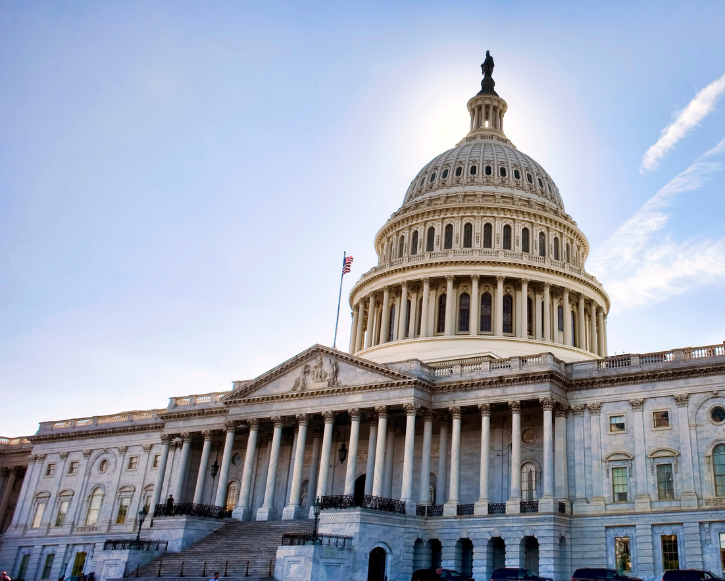 The United States Capitol building with its large dome illuminated by the sun against a clear blue sky.