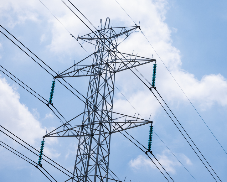 Metal electrical transmission tower with power lines against a blue sky with clouds.