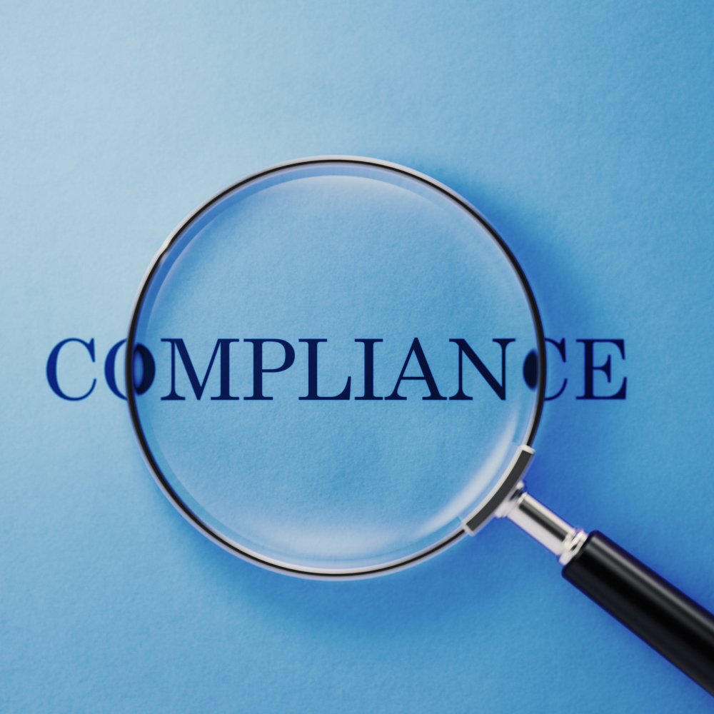 Magnifying glass enlarging the word 'COMPLIANCE' on a blue background.