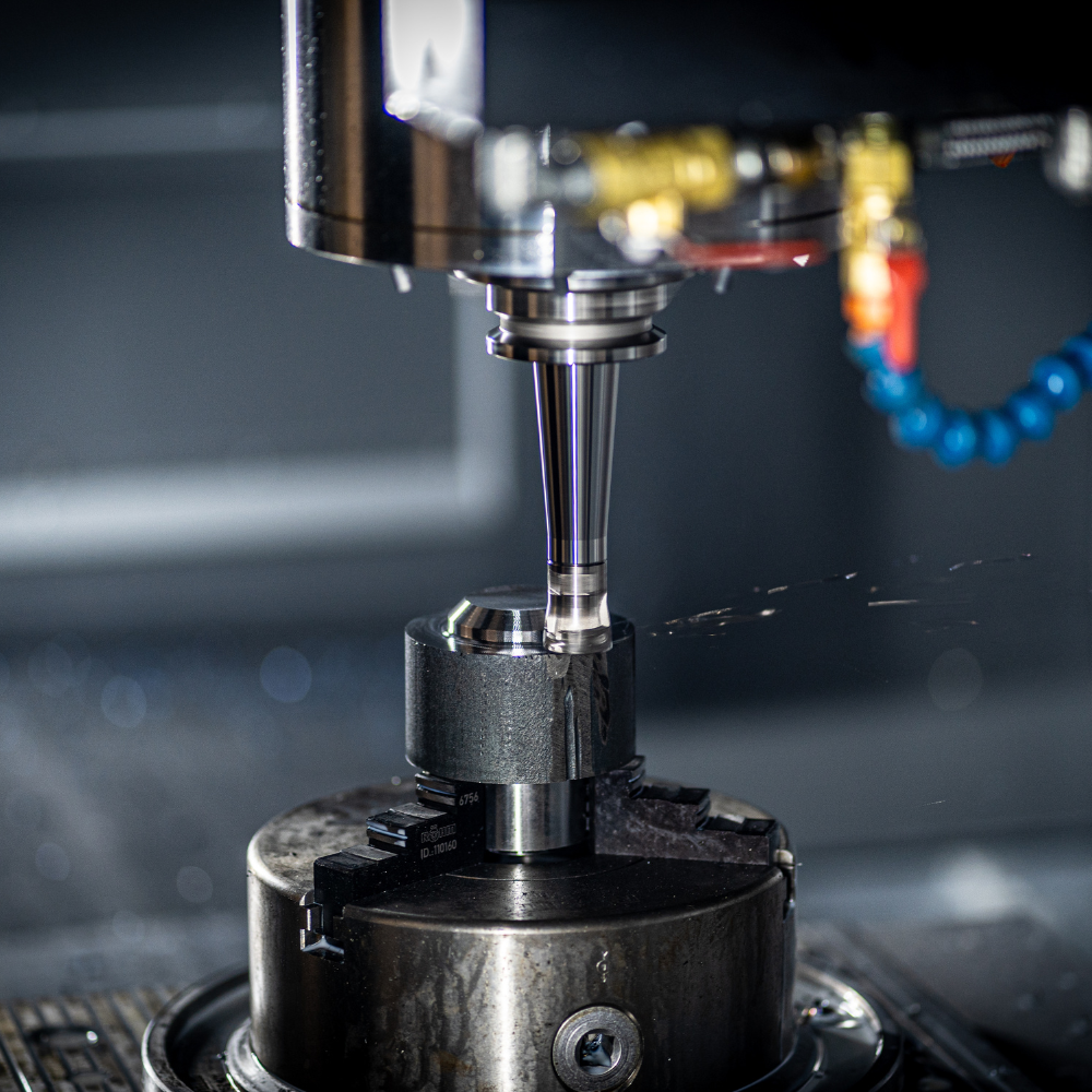 Close-up of CNC machine drilling metal workpiece with coolant spray in an industrial setting.