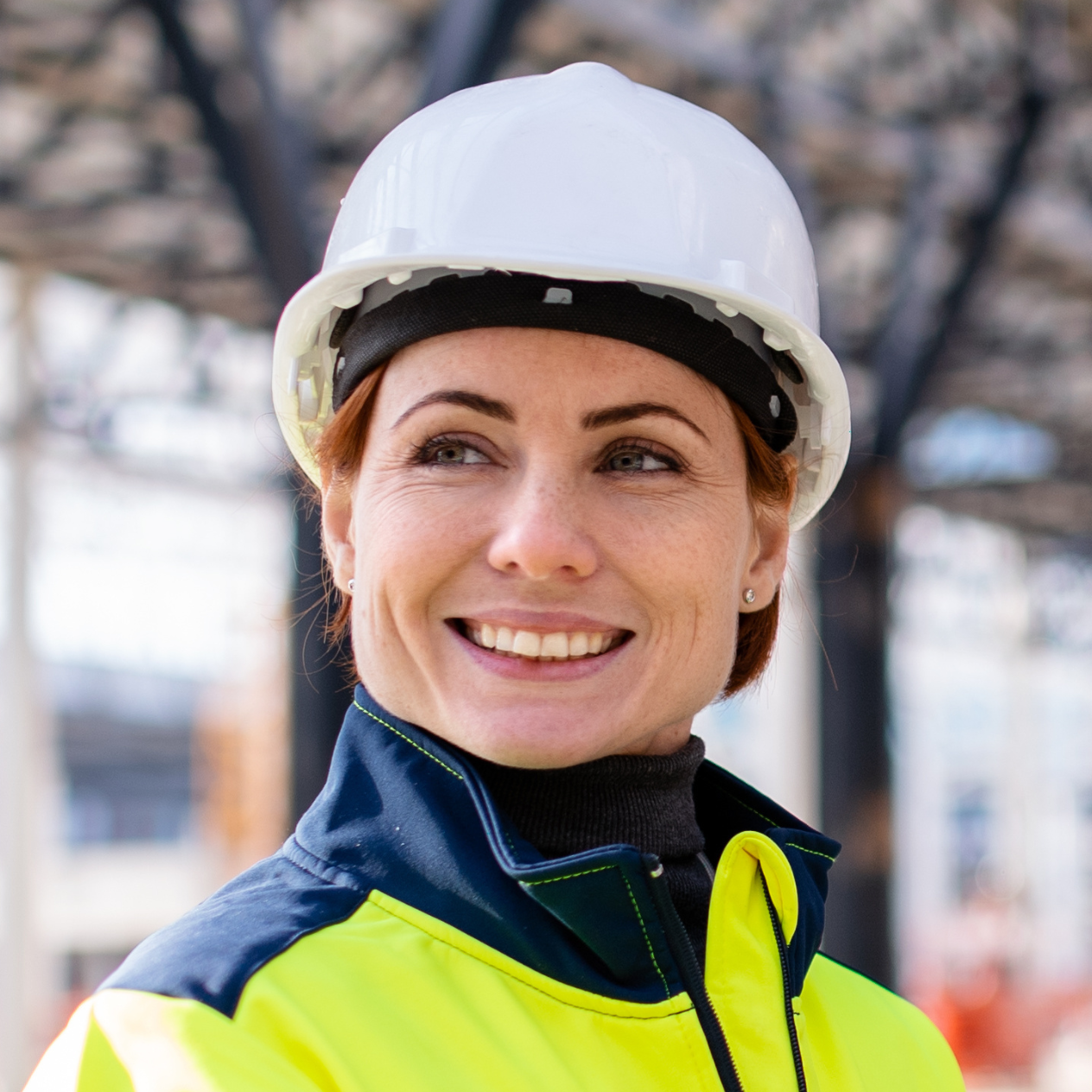Smiling woman in a white hard hat and hi-vis jacket on a construction site