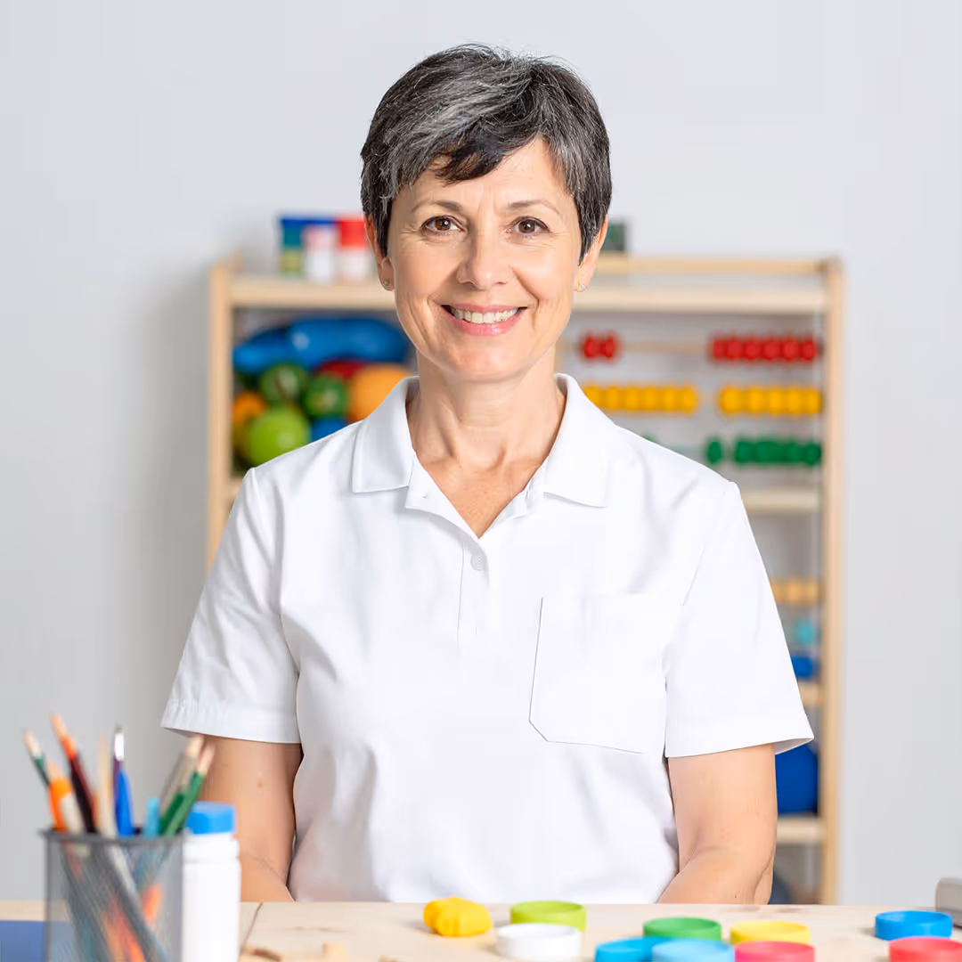 Ergotherapeut (46) zeigt Assessments und Timer am Tisch; aufgeräumte Praxis, kompetentes Porträt.