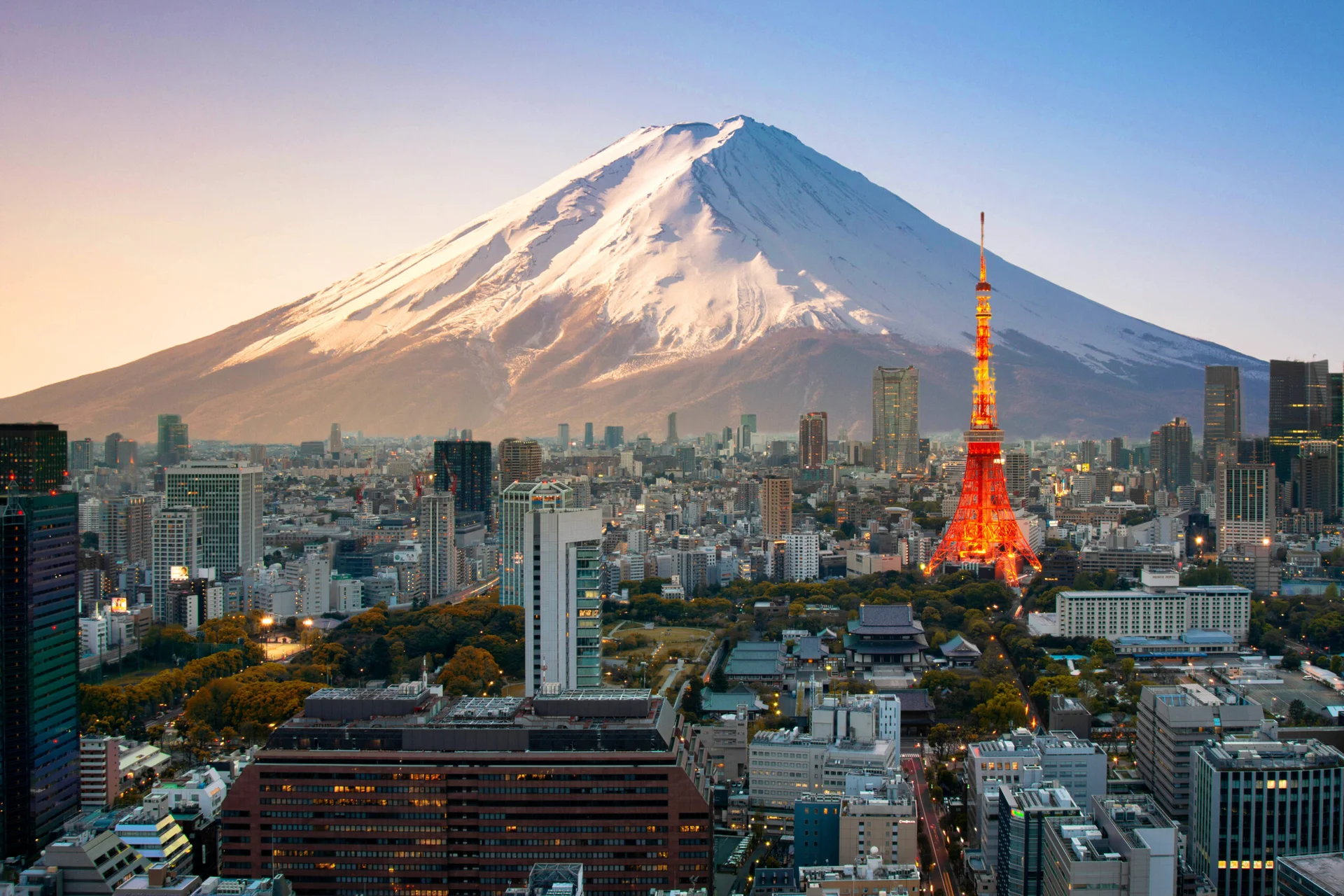 Tokyo city skyline with illuminated Tokyo Tower and snowy Mount Fuji in the background at dusk.