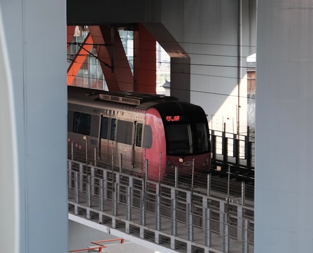 Modern pink and silver train moving on elevated tracks under a bridge structure with steel supports.
