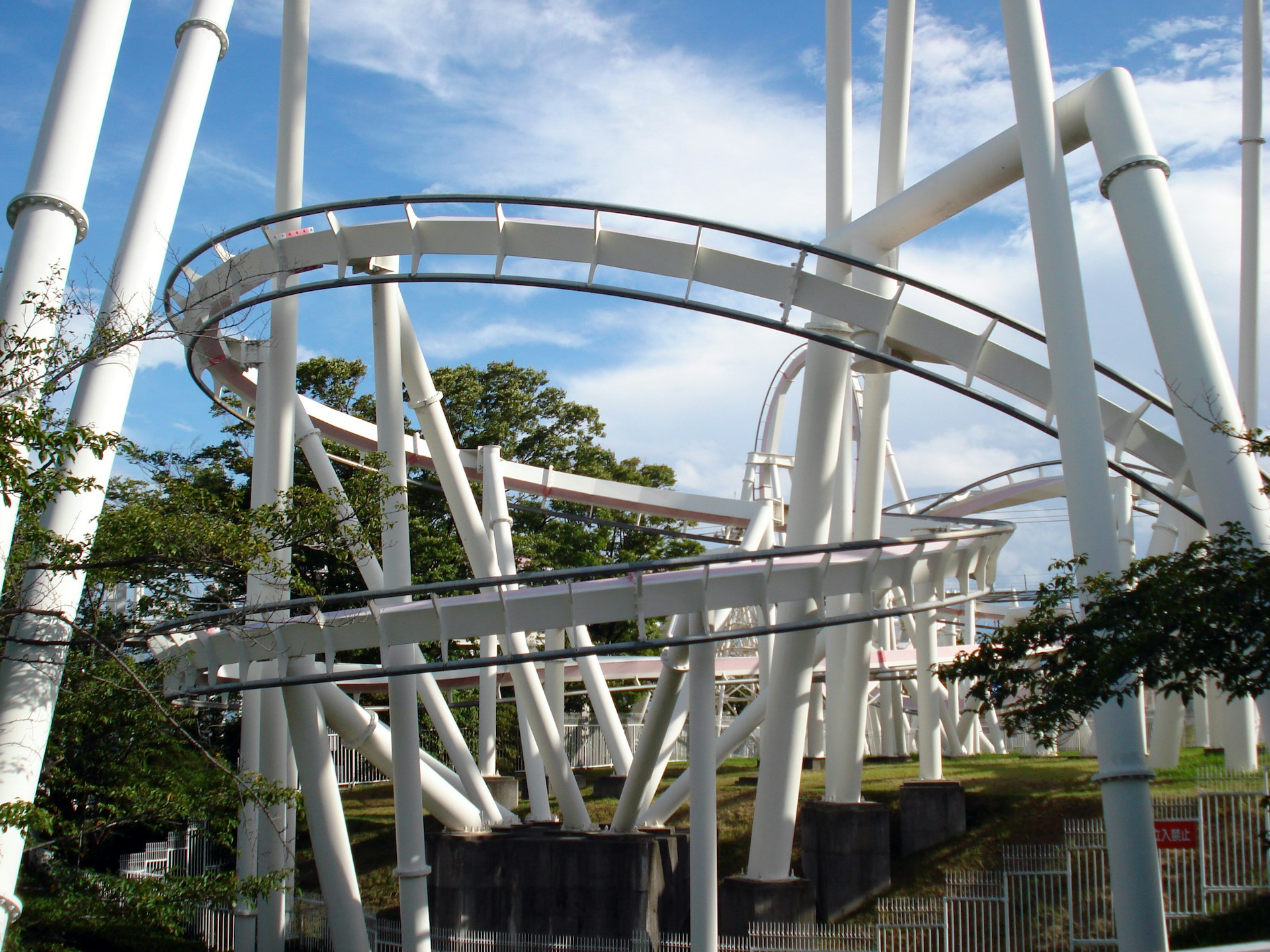 Curved white roller coaster track supported by large white beams against a partly cloudy blue sky.