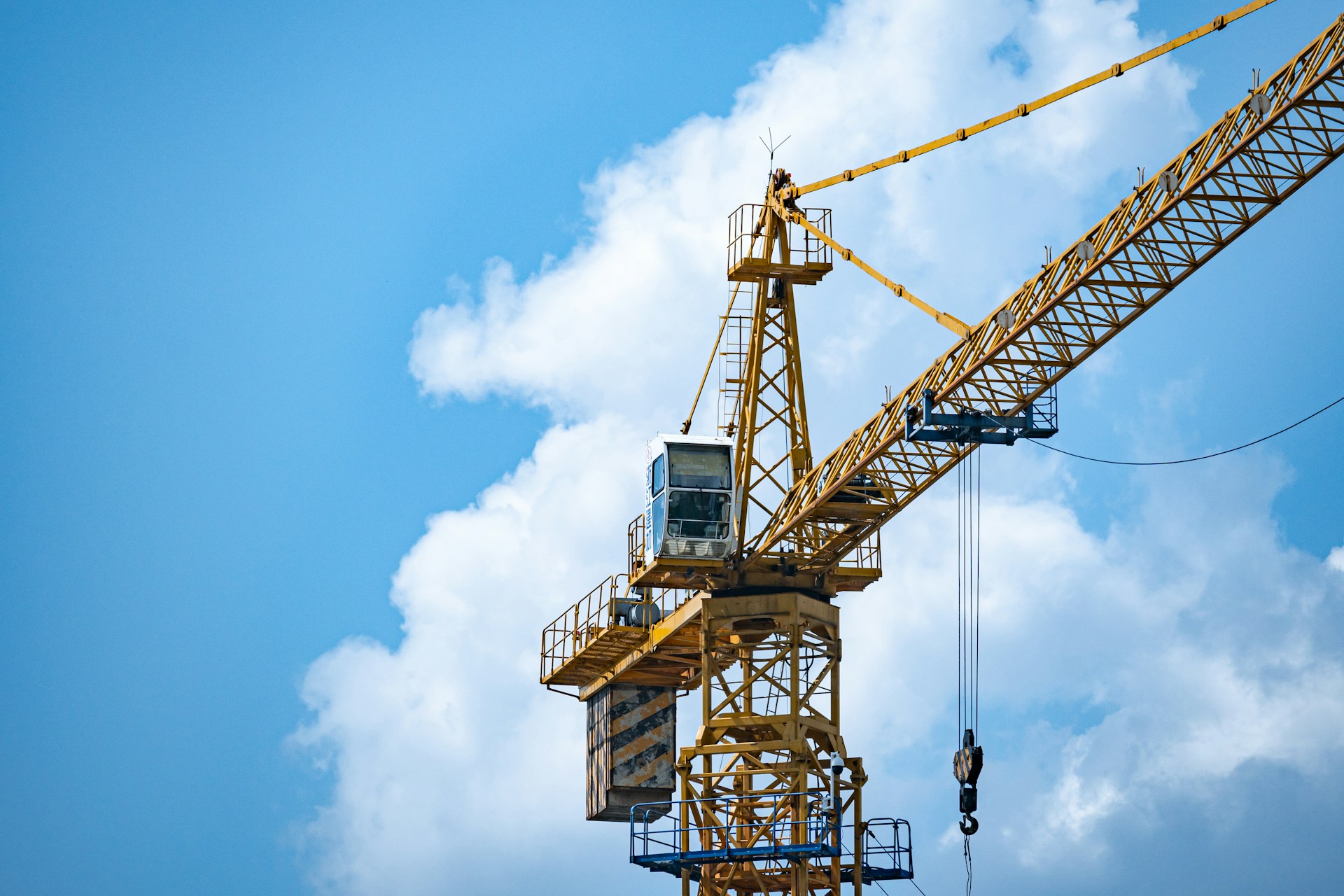 Yellow construction crane against a blue sky with scattered white clouds.