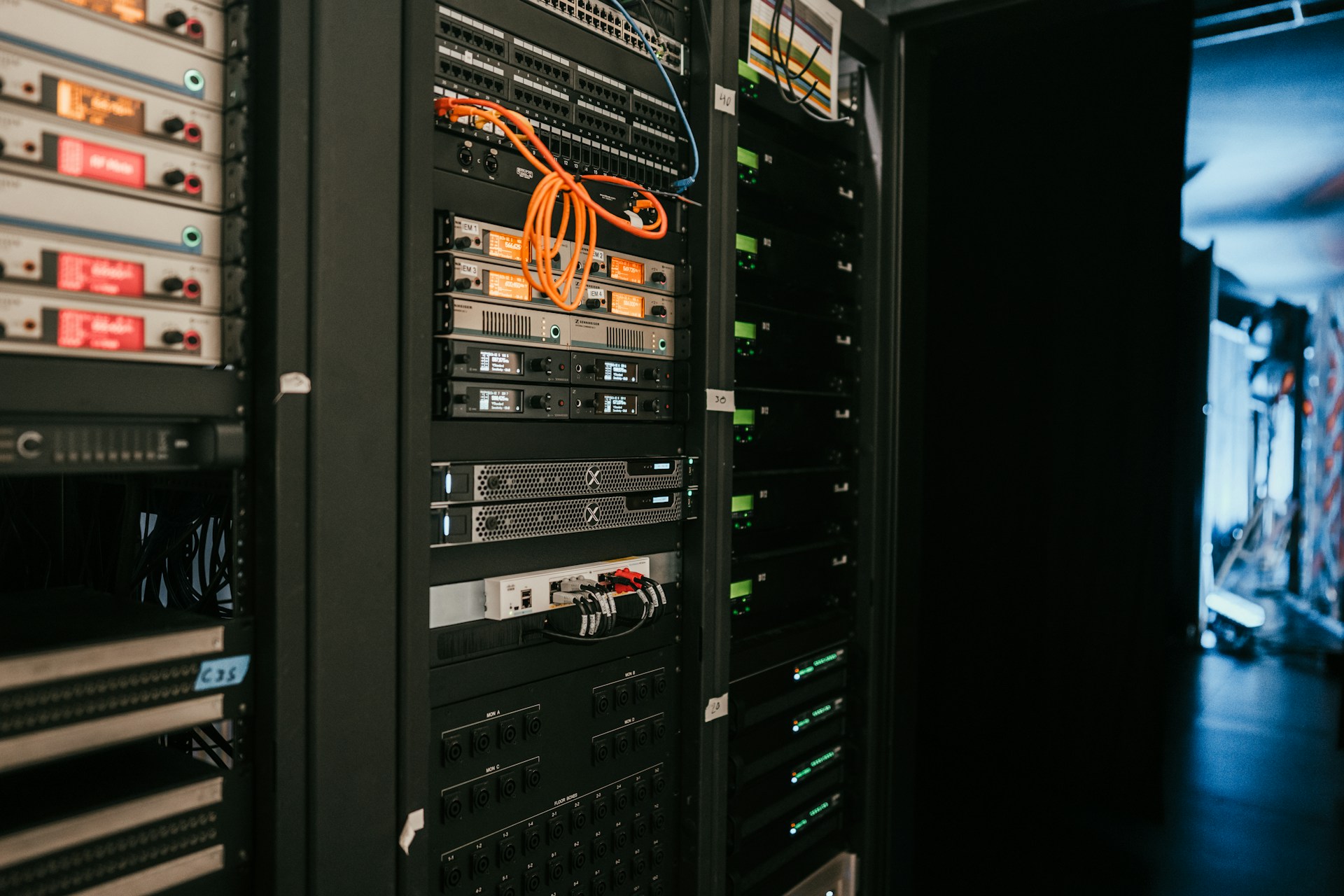 Close-up of server racks with networking equipment, cables, and audio devices in a dimly lit data center or studio.