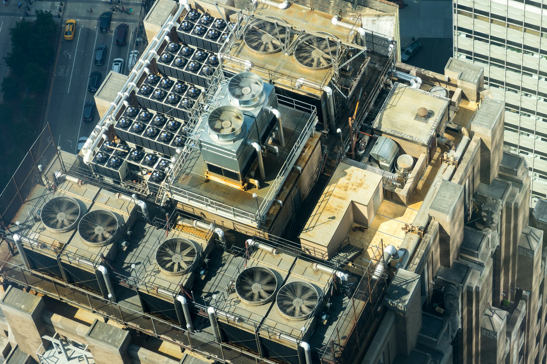 Aerial view of a building rooftop filled with multiple large industrial HVAC cooling units and ventilation fans.