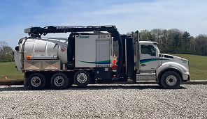White hydro excavation truck with large vacuum tank parked on gravel beside a grassy field.
