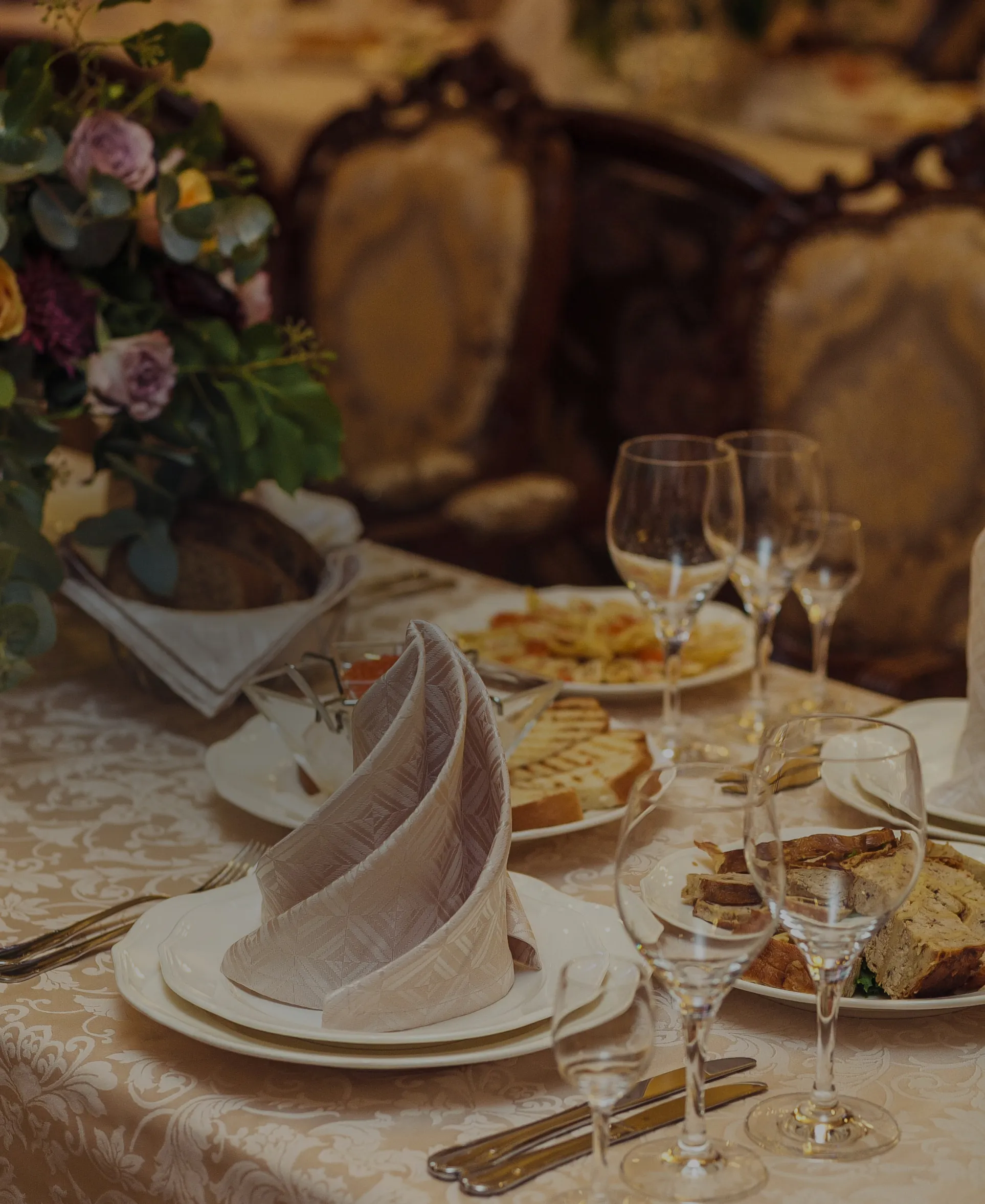Elegant dinner table set with folded napkins, wine glasses, plates of food, and floral centerpieces in a luxurious dining room.