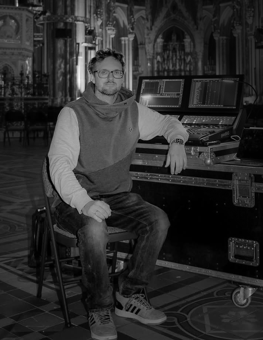 Black and white close-up portrait of a young man with medium-length hair, looking directly at the camera with a neutral expression.