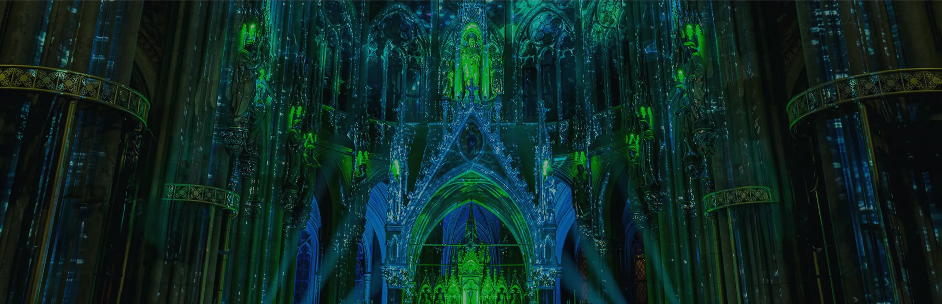 Colorful light projection illuminating the interior of a grand Gothic cathedral with green and blue tones highlighting the arches and statues.