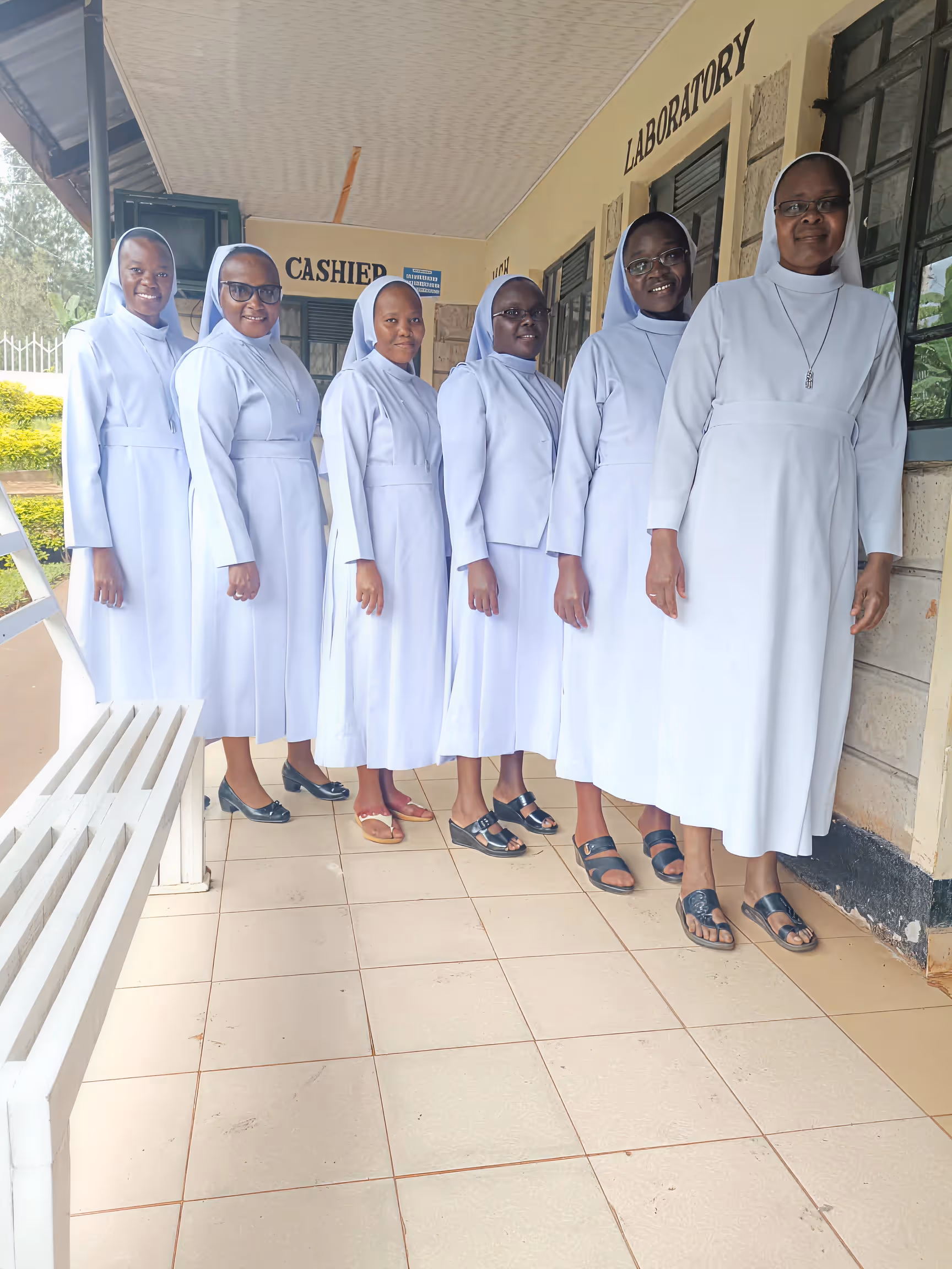 Six nuns standing in a line inside a building corridor with signs reading 'CASHIER' and 'LABORATORY' in the background.