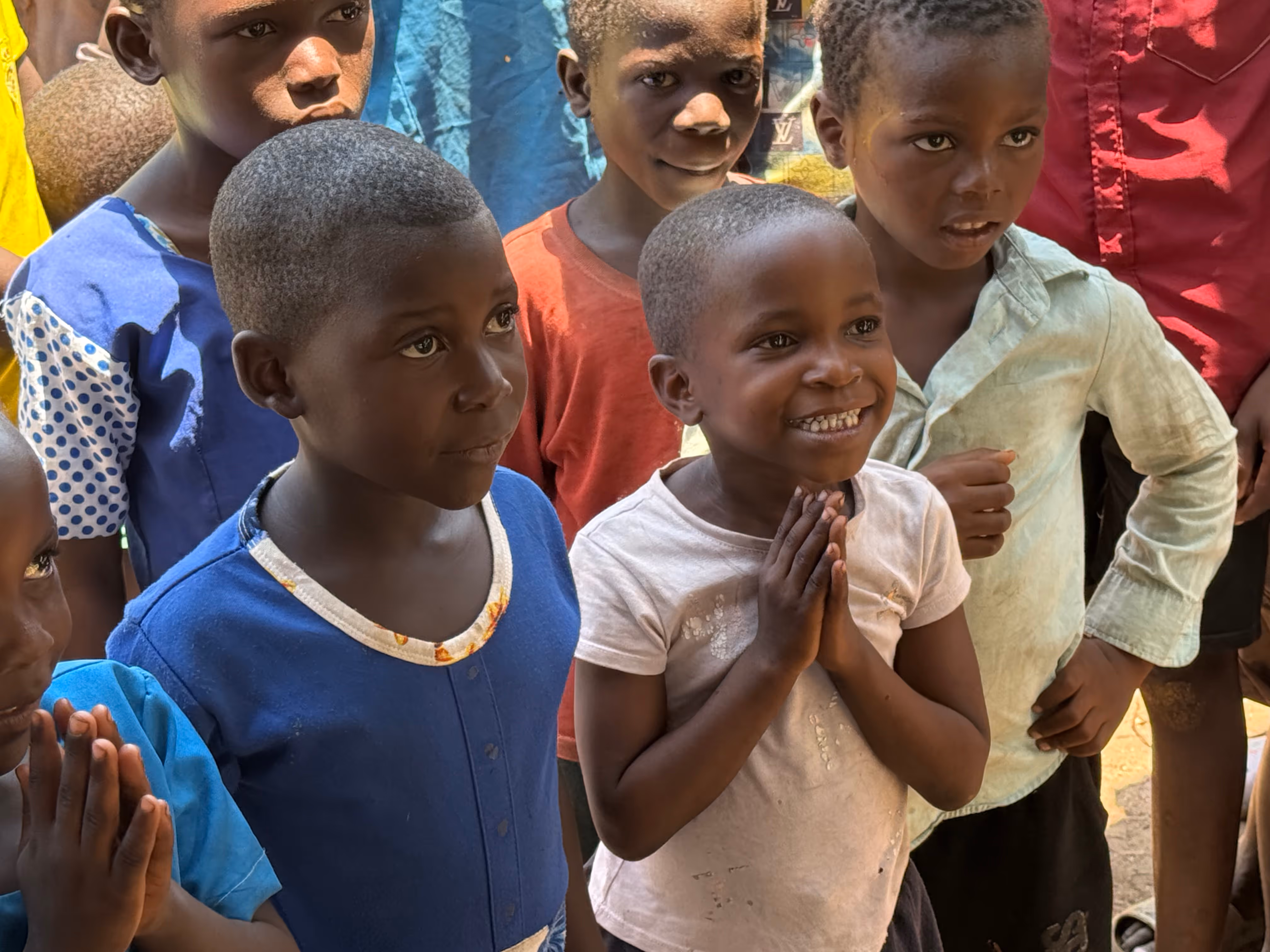 Group of smiling and attentive children standing closely together outdoors.
