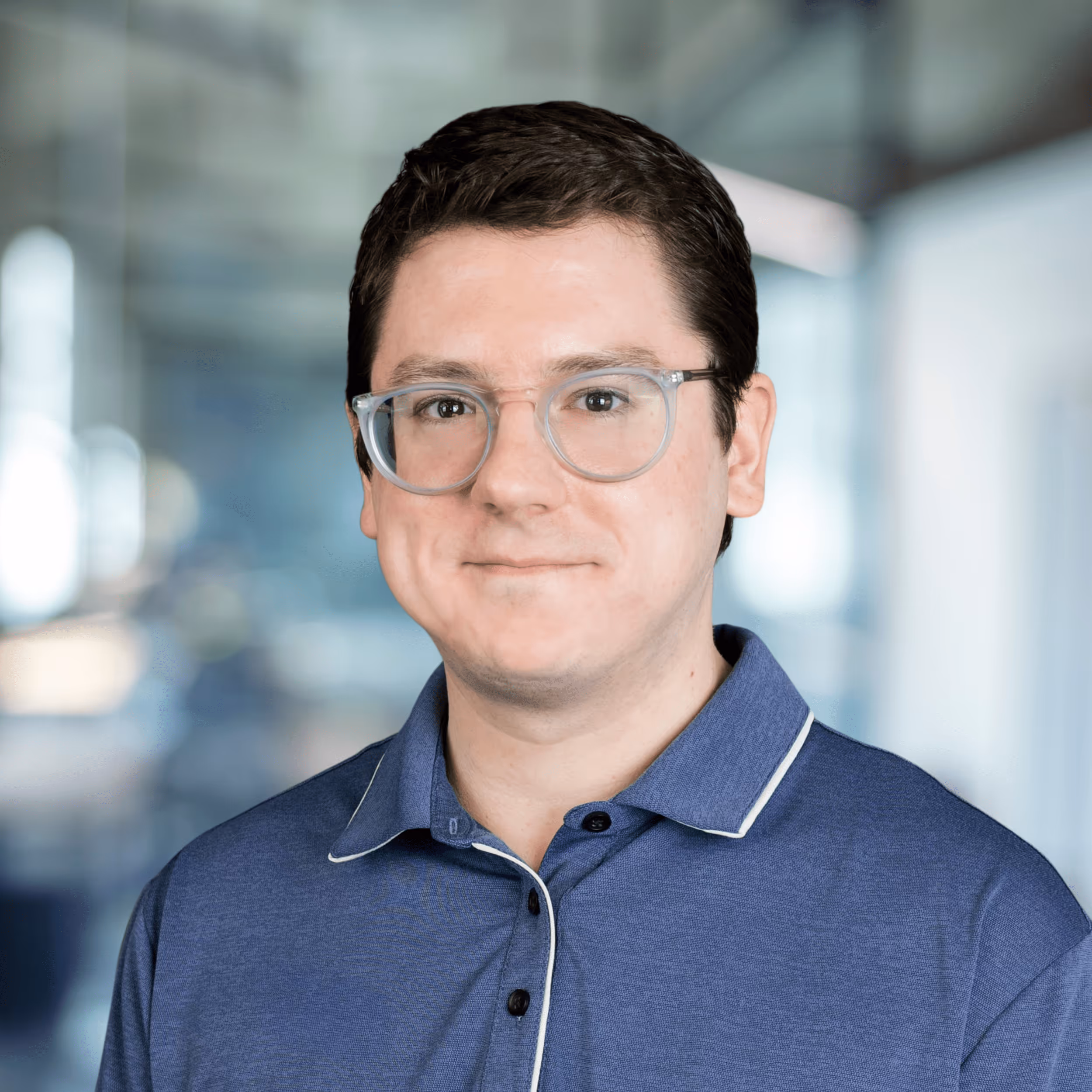 Smiling woman with long red hair wearing a maroon blazer and blue top in a modern office setting.