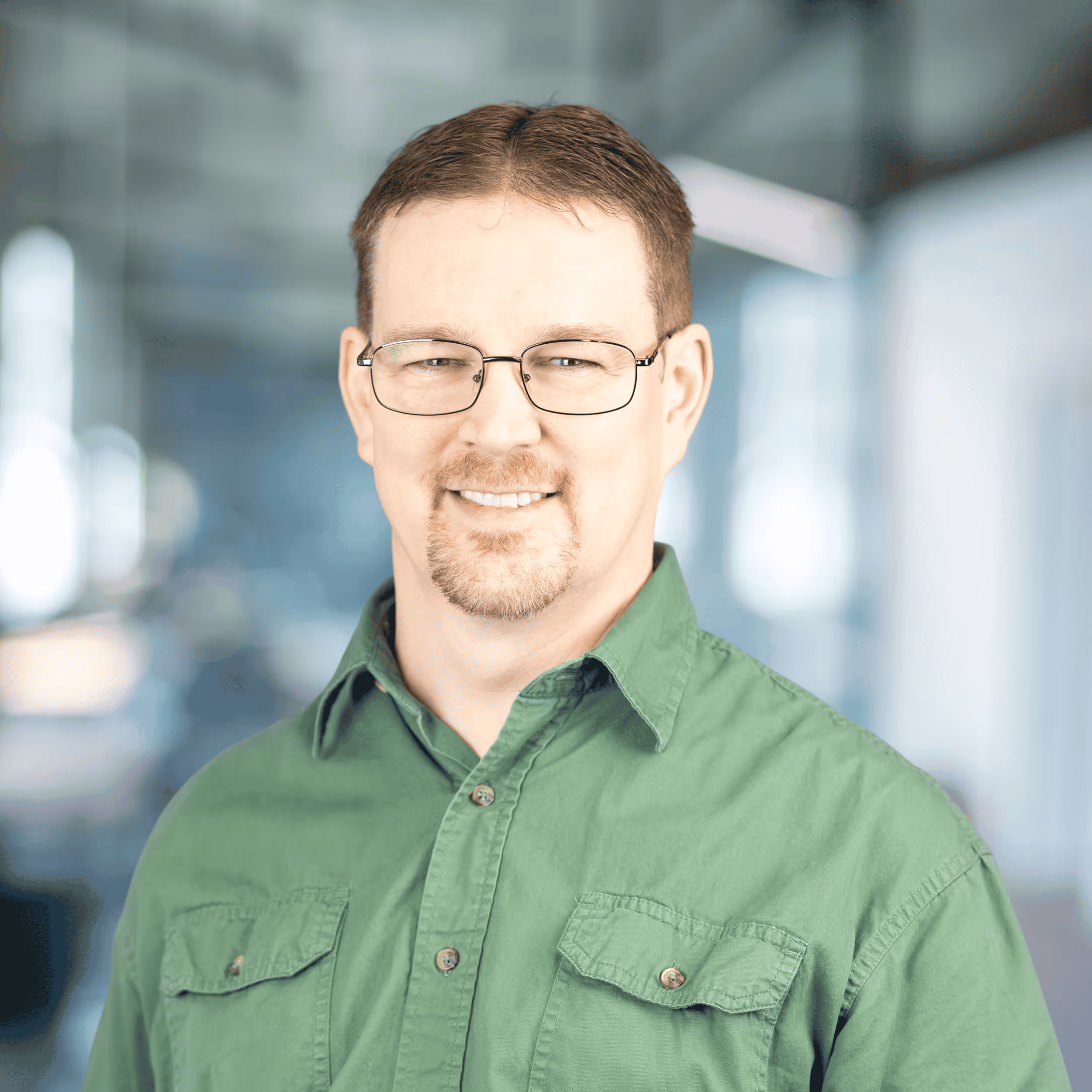 Smiling woman with long red hair wearing a maroon blazer and blue top in a modern office setting.