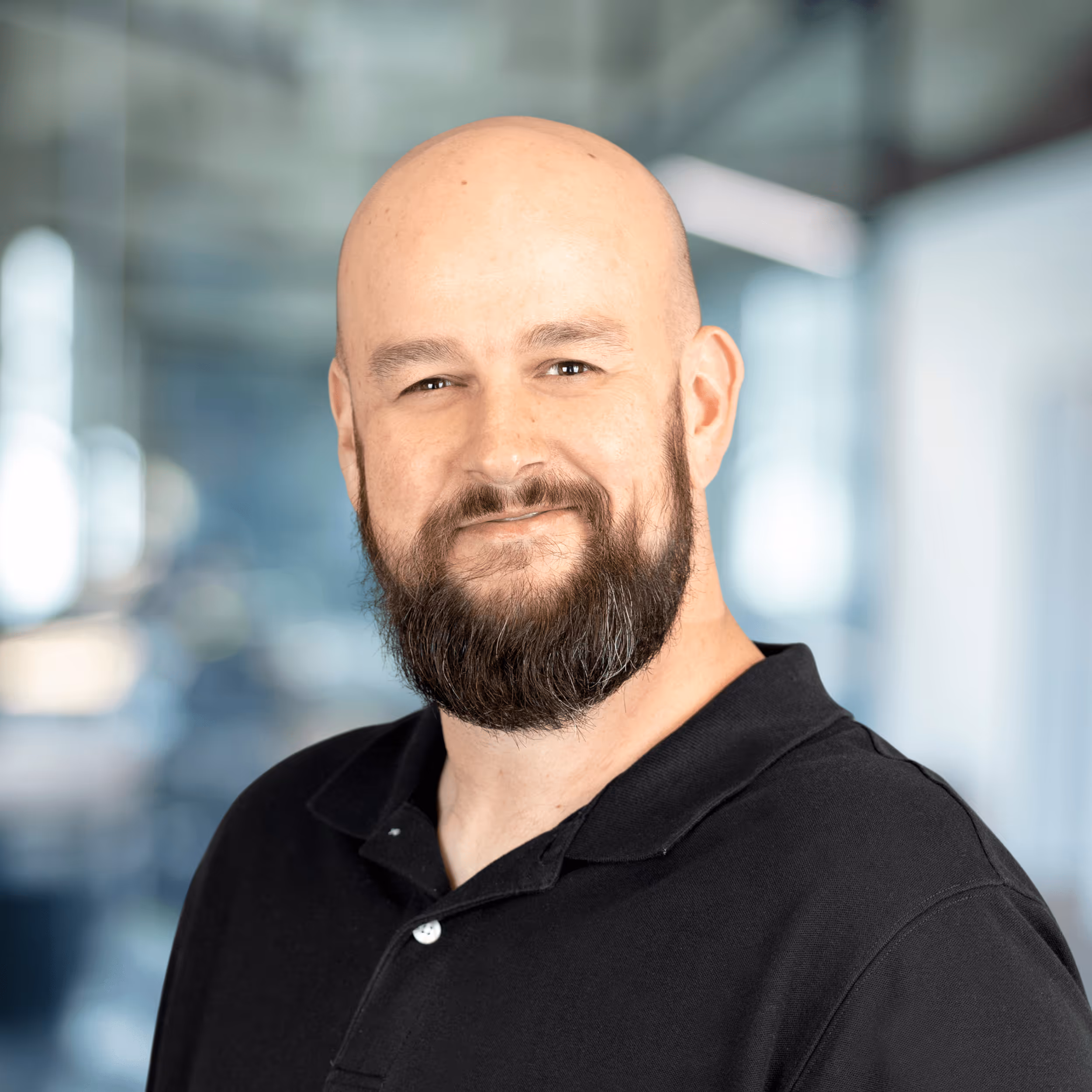 Smiling woman with long red hair wearing a maroon blazer and blue top in a modern office setting.