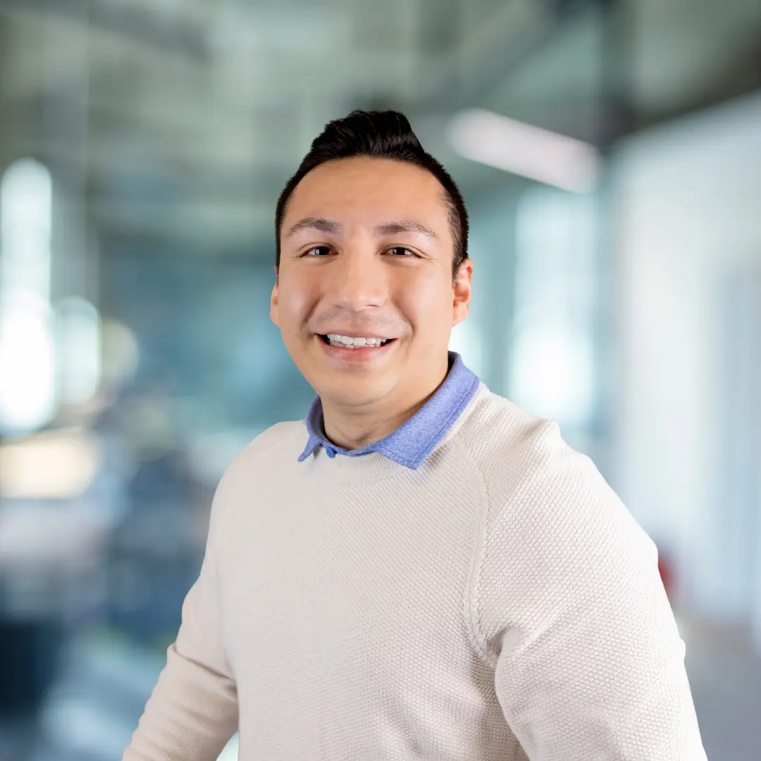 Smiling woman with long red hair wearing a maroon blazer and blue top in a blurred office background.