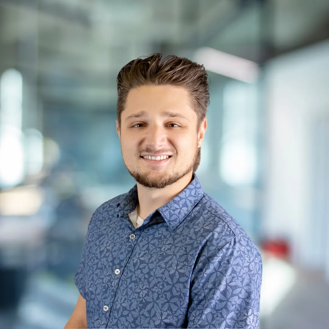 Smiling woman with shoulder-length wavy brown hair wearing a black top with ruffled sleeves.
