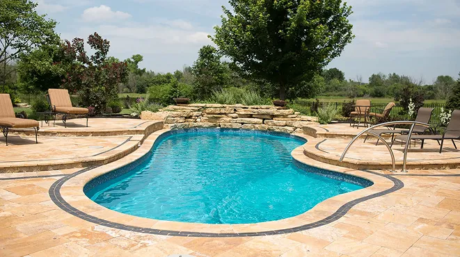 A pool surrounded by chairs and a stone patio.