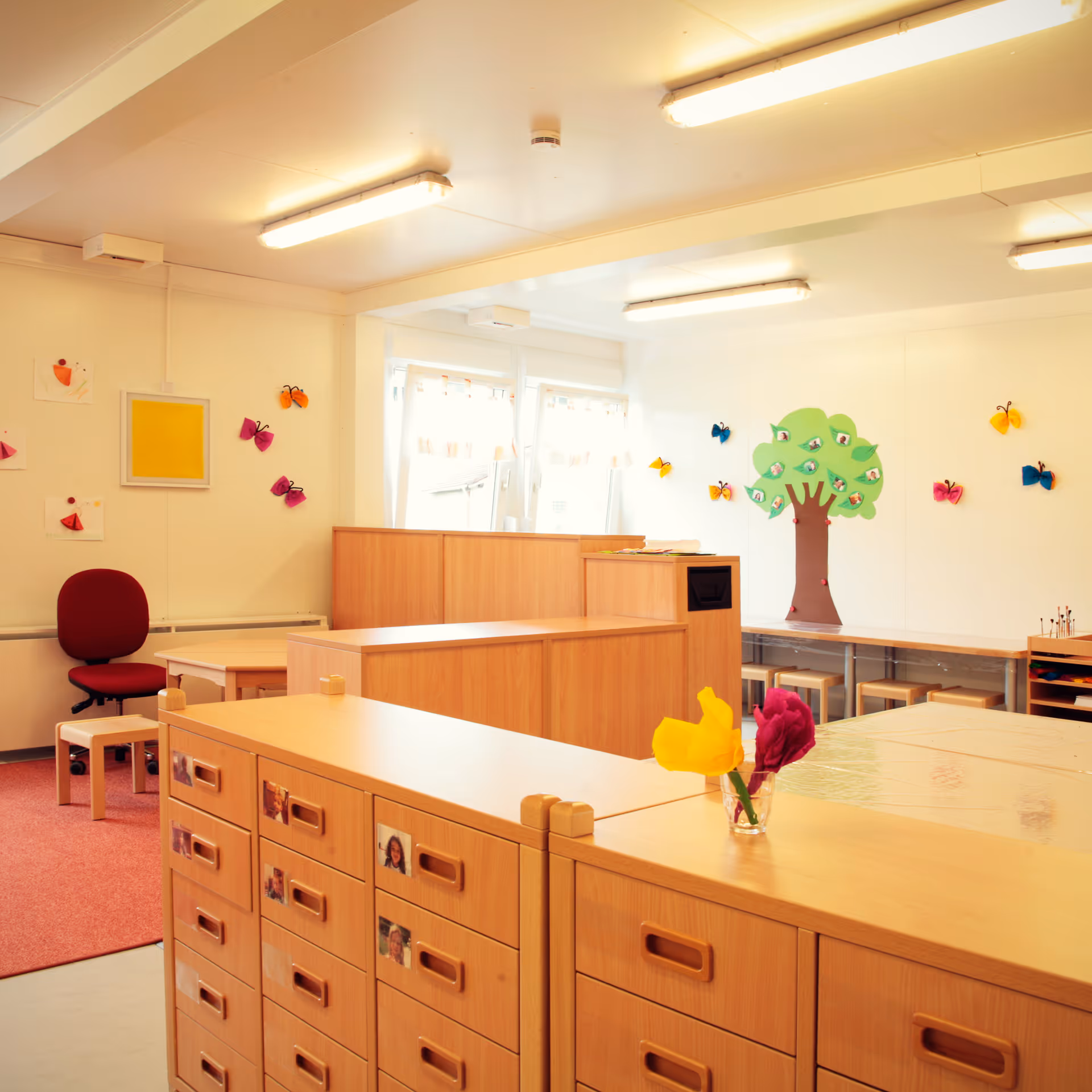 Hell eingerichteter Kindergartenraum mit bunten Schmetterlingsdekorationen und einem Baum aus Papier an der Wand.