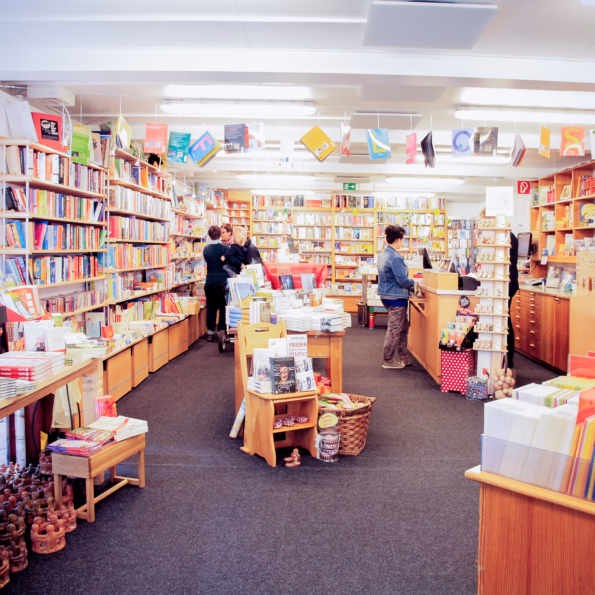Innenansicht einer gut beleuchteten Buchhandlung mit mehreren Besuchern, die zwischen den Bücherregalen und Kassenbereich stöbern.