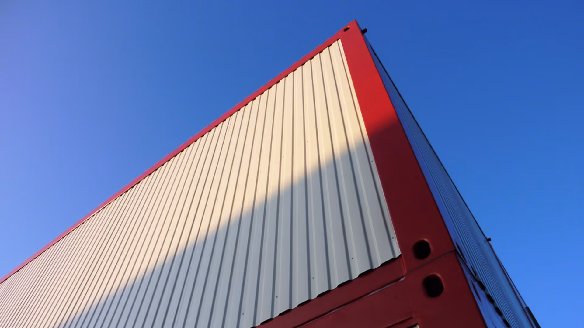 Ansicht der Oberseite eines rot-weißen Containergebäudes vor klarem blauem Himmel.