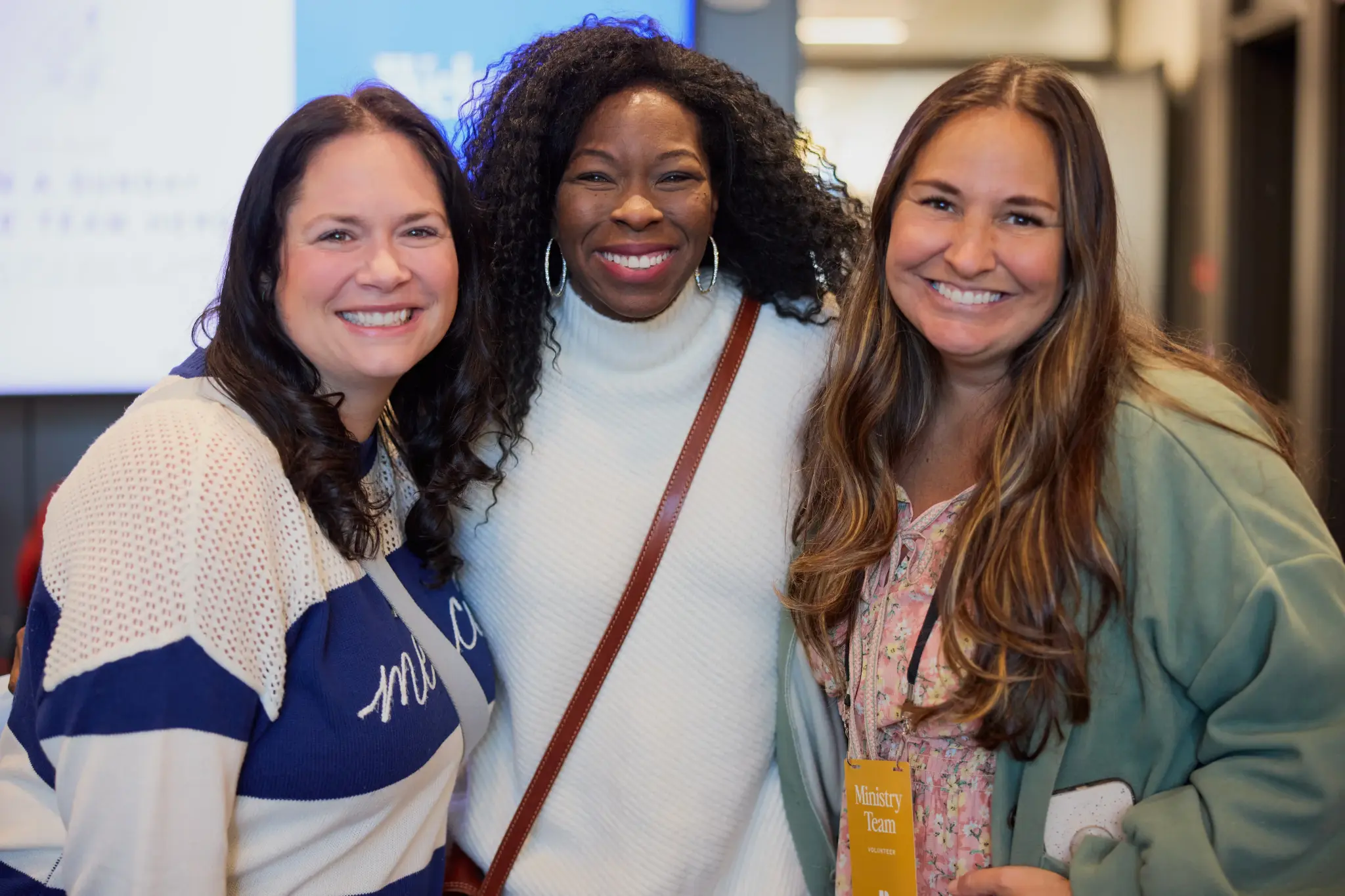 Three women smiling together at an indoor event.